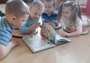 Szymek, Miłosz, Adaś i Zosia oglądają książkę z bajkami.